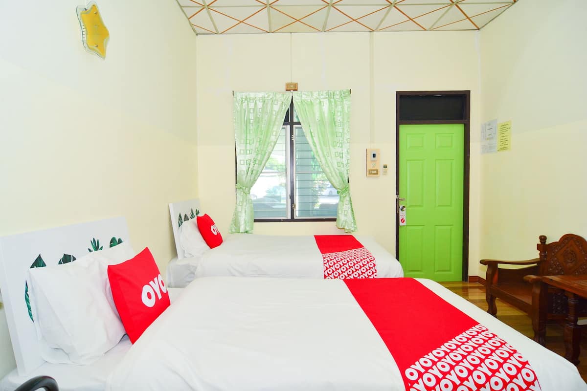 A hotel room with two beds, a green door, and a window with green curtains.
