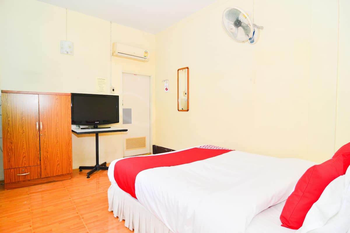 A hotel room with a bed, a TV on a stand, a wardrobe, and a wall-mounted fan.