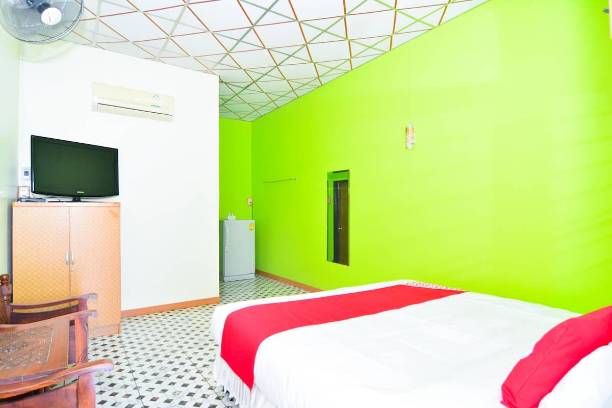 A room with a bed, a television on a cabinet, a small refrigerator, and a door.