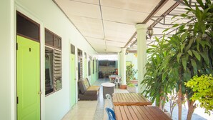 A covered corridor with a wooden table and chairs, a green door, and a seating area with a sofa and a small table.