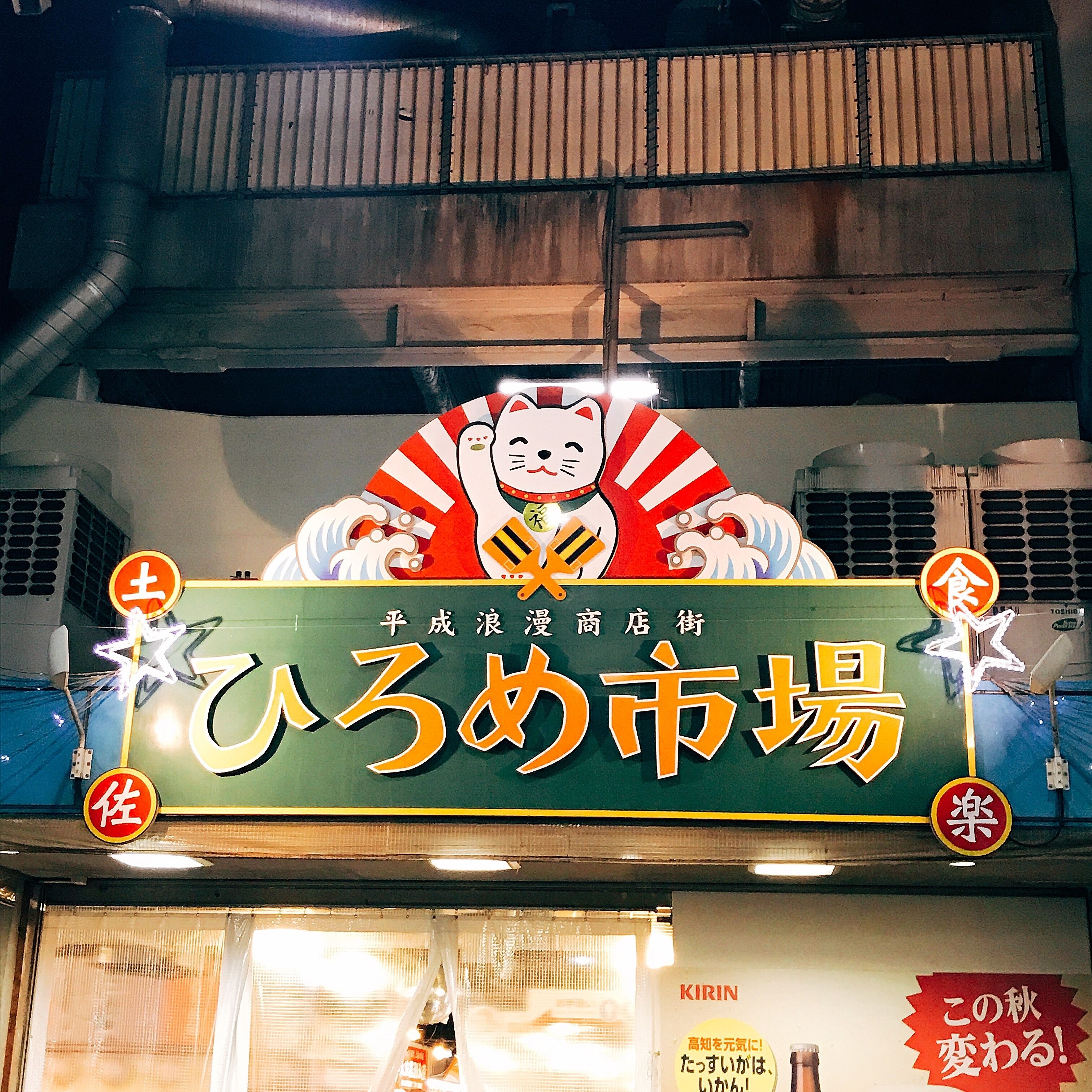 A storefront with a large sign featuring a cat and Japanese characters, indicating a market or shop.