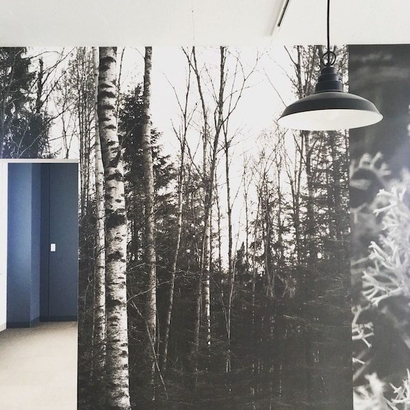 A room with a large window displaying a forest scene, a hanging pendant light, and a blue door.