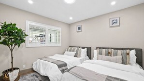 A bedroom with two beds, a potted plant, and a window with blinds. - The Farmhouse Retreat (Midway City)