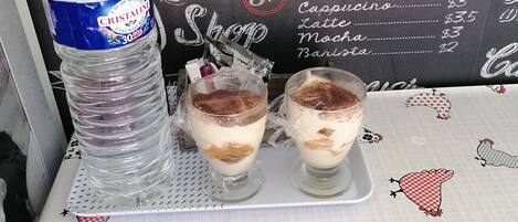 Eine Kaffeekarte mit Preisen, eine Wasserflasche und zwei mehrschichtige Getränke auf einem Tisch.