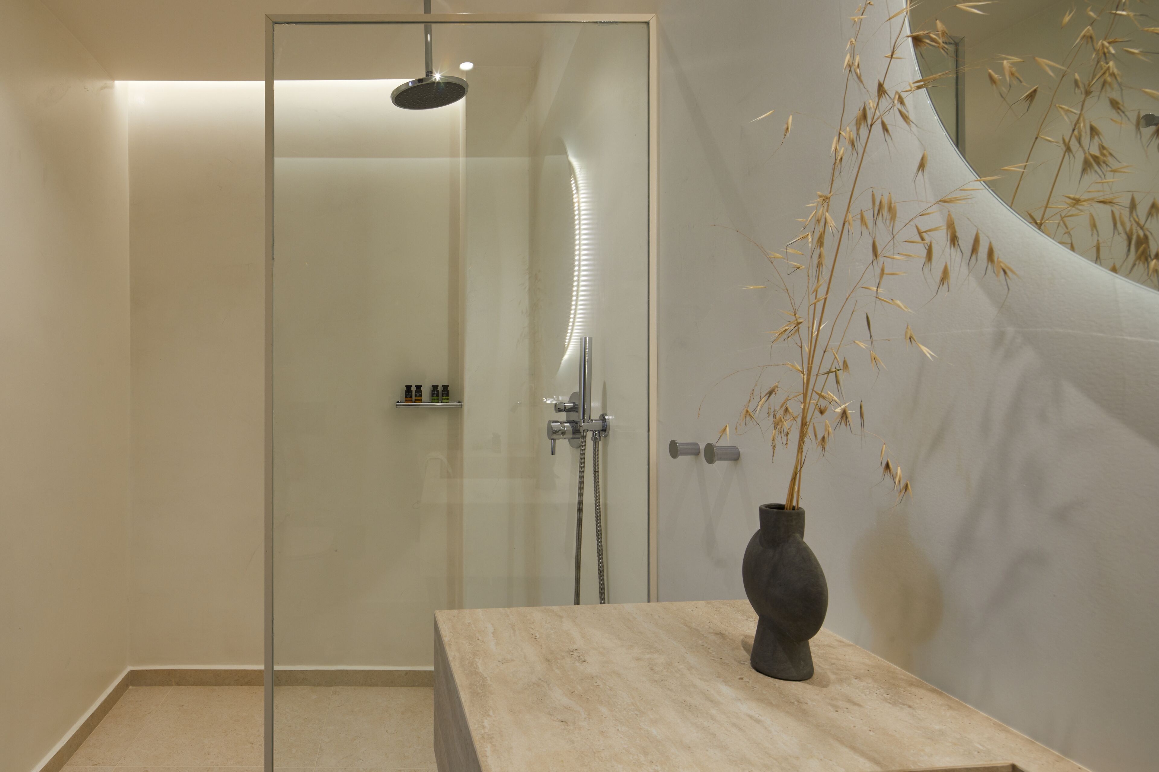 A modern bathroom with a glass-enclosed shower, a marble countertop, and a vase with dried plants.