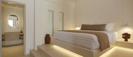 A modern bedroom with a large bed, a bedside table, a mirror, and a staircase leading to an adjacent bathroom.