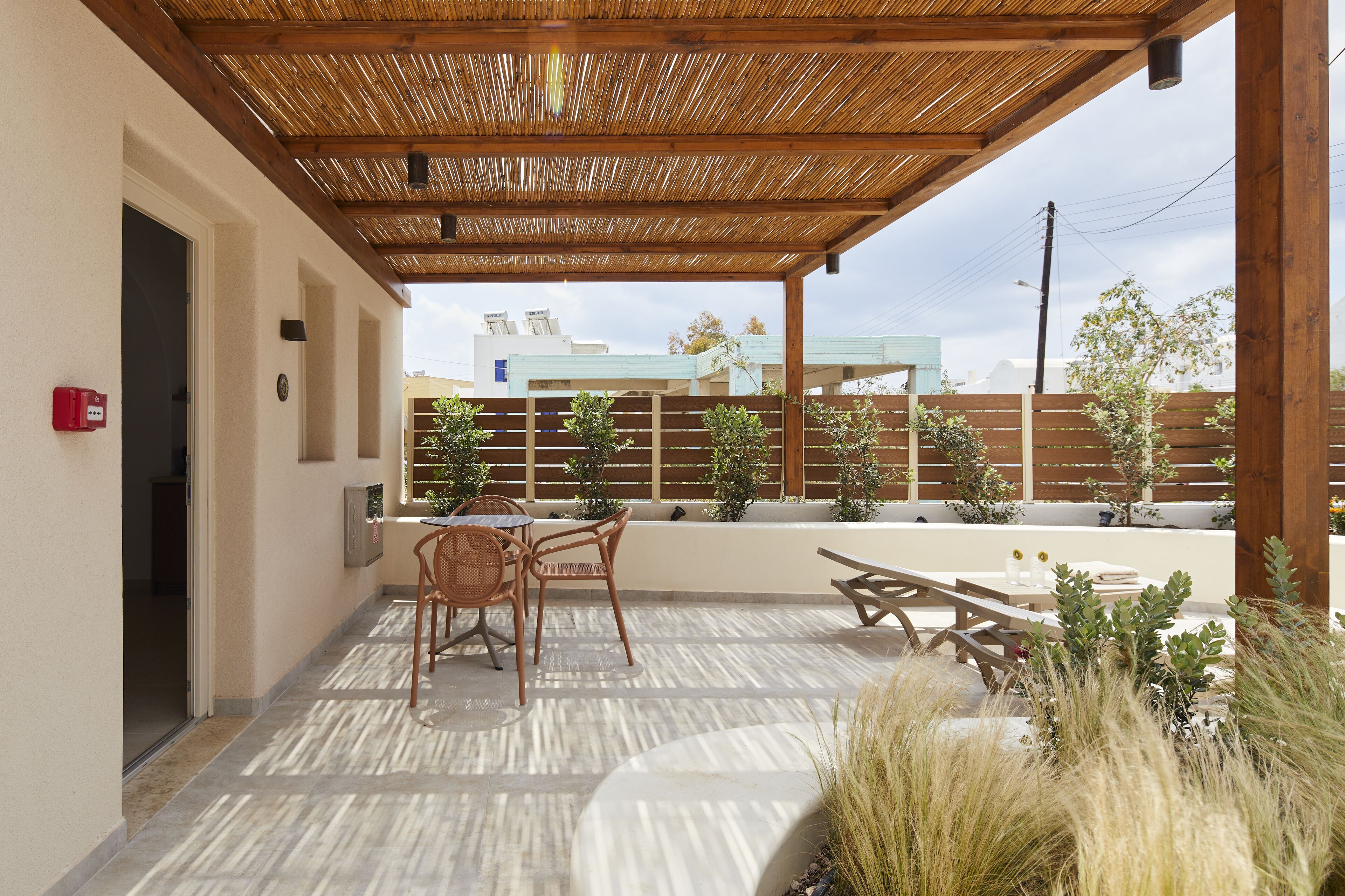 Ein überdachter Patio-Bereich mit Tisch und Stühlen, einer Holzbank und Kübelpflanzen.