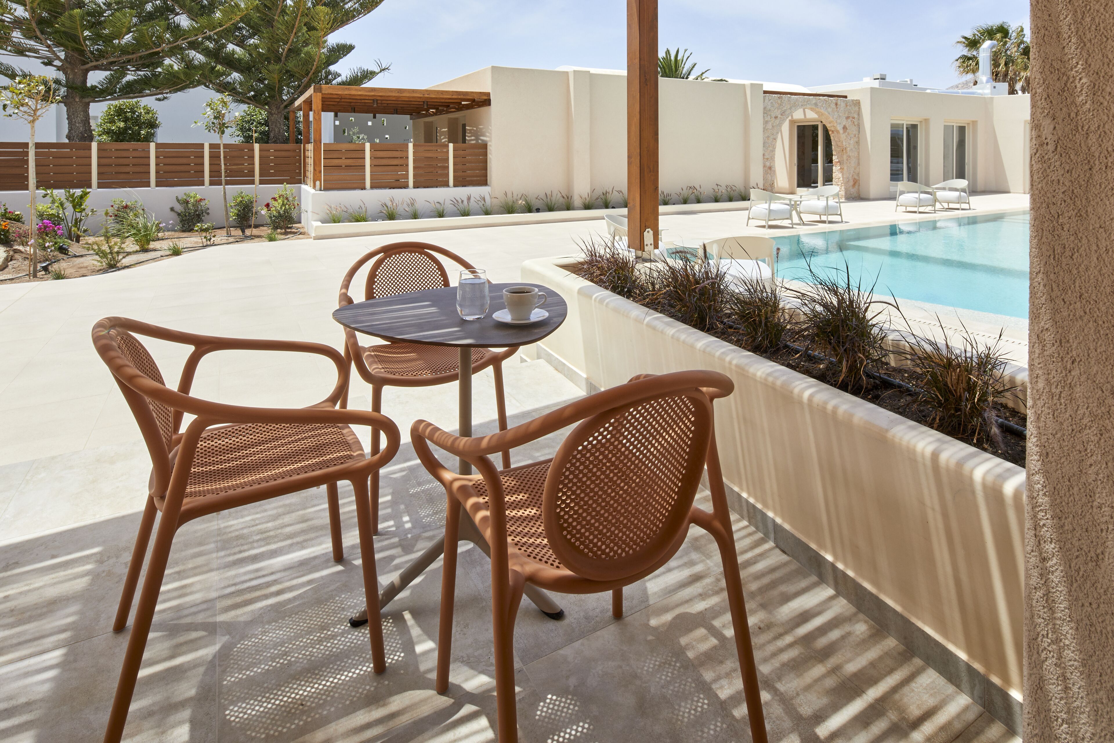 An outdoor seating area with wicker chairs and a table, a pool, and a white building with a wooden fence.