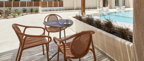 An outdoor seating area with wicker chairs and a table, a pool, and a white building with a wooden fence.