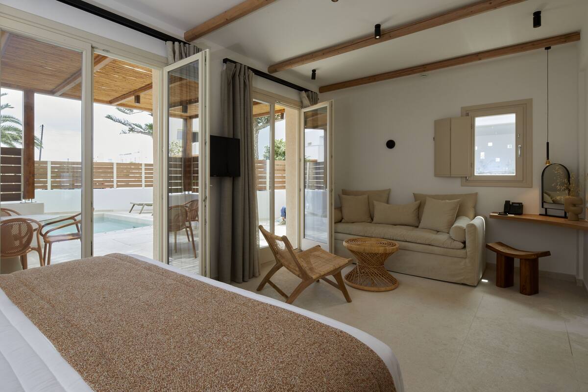 A spacious bedroom with a large bed, a sofa, and a dining area with a pool view.