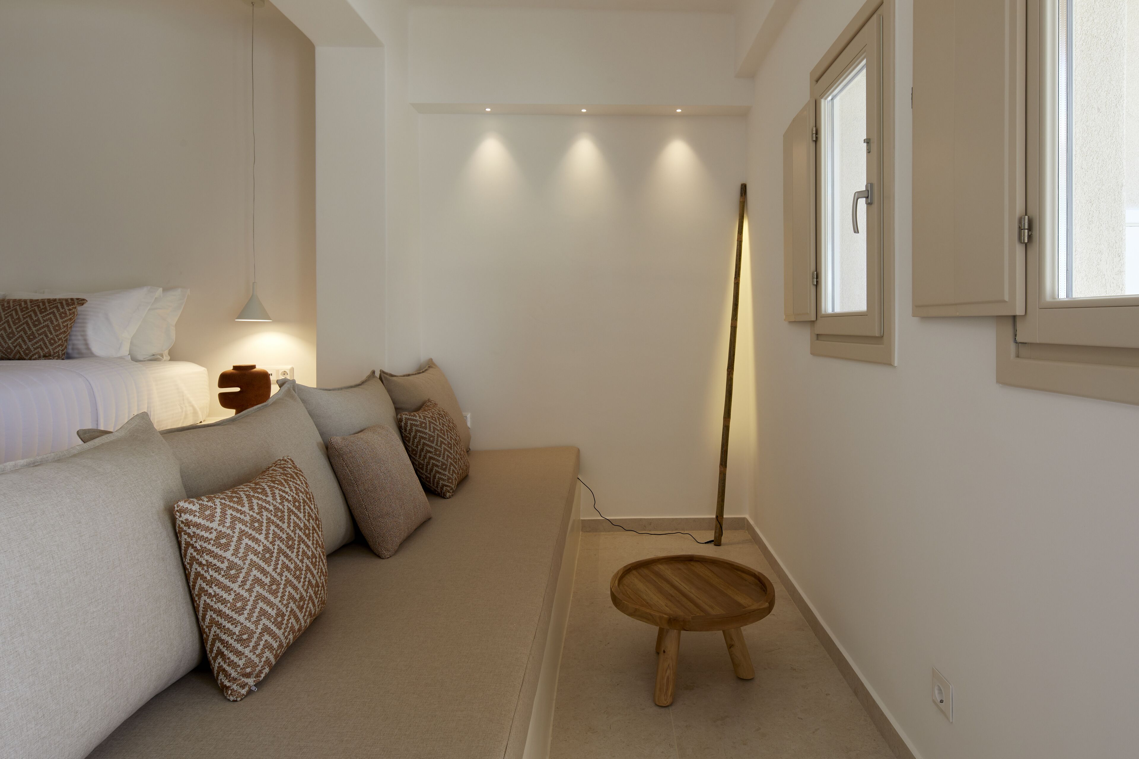 Une chambre à coucher avec un lit, une table de chevet, une lampe de chevet, une lampe sur pied et un petit tabouret en bois.