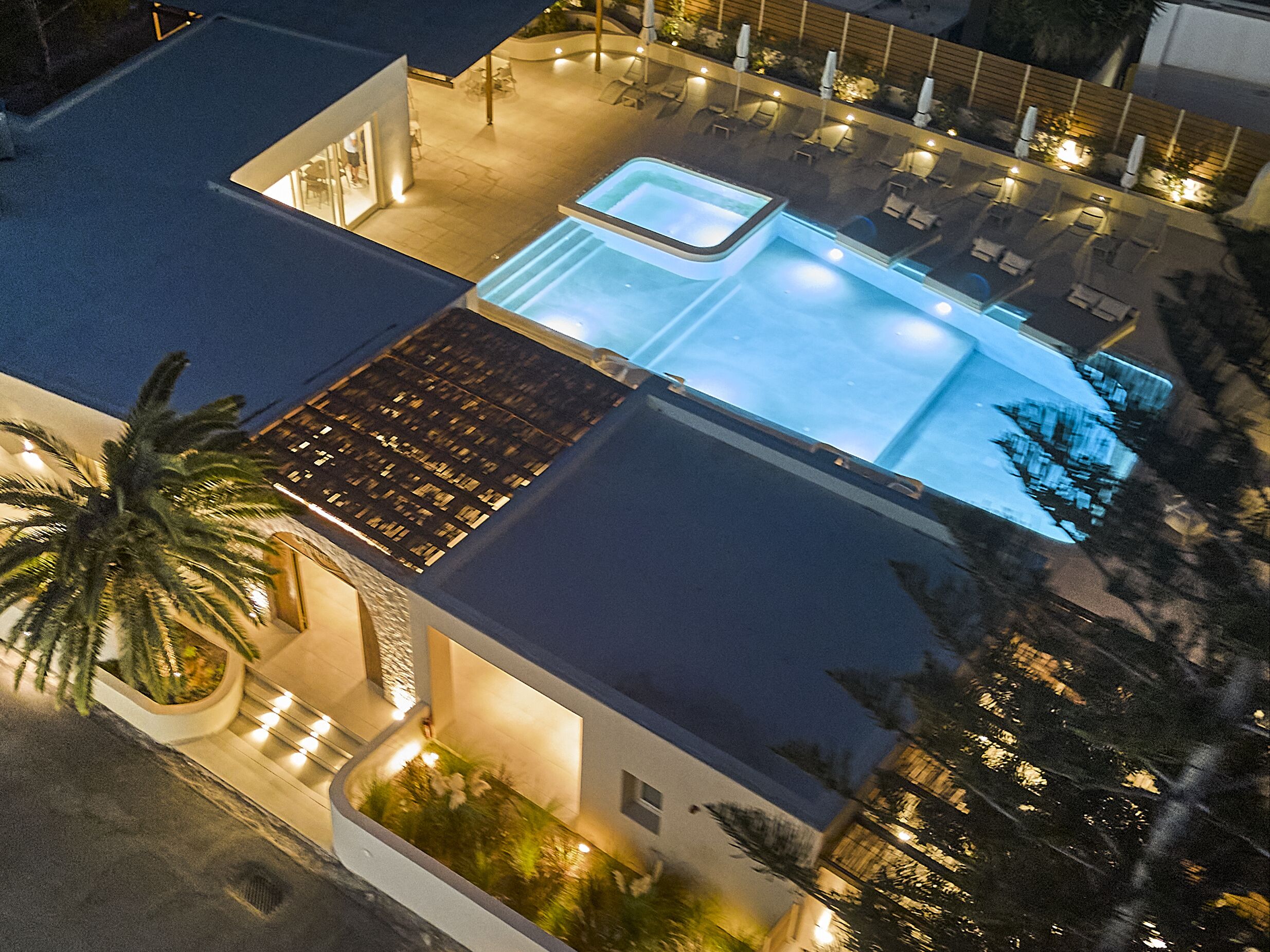 Vista aérea de un hotel con piscina, sillas de descanso y un jardín ajardinado.