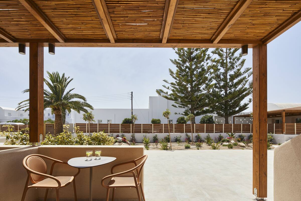 An outdoor patio with two wicker chairs and a table, overlooking a landscaped garden and a building in the background.