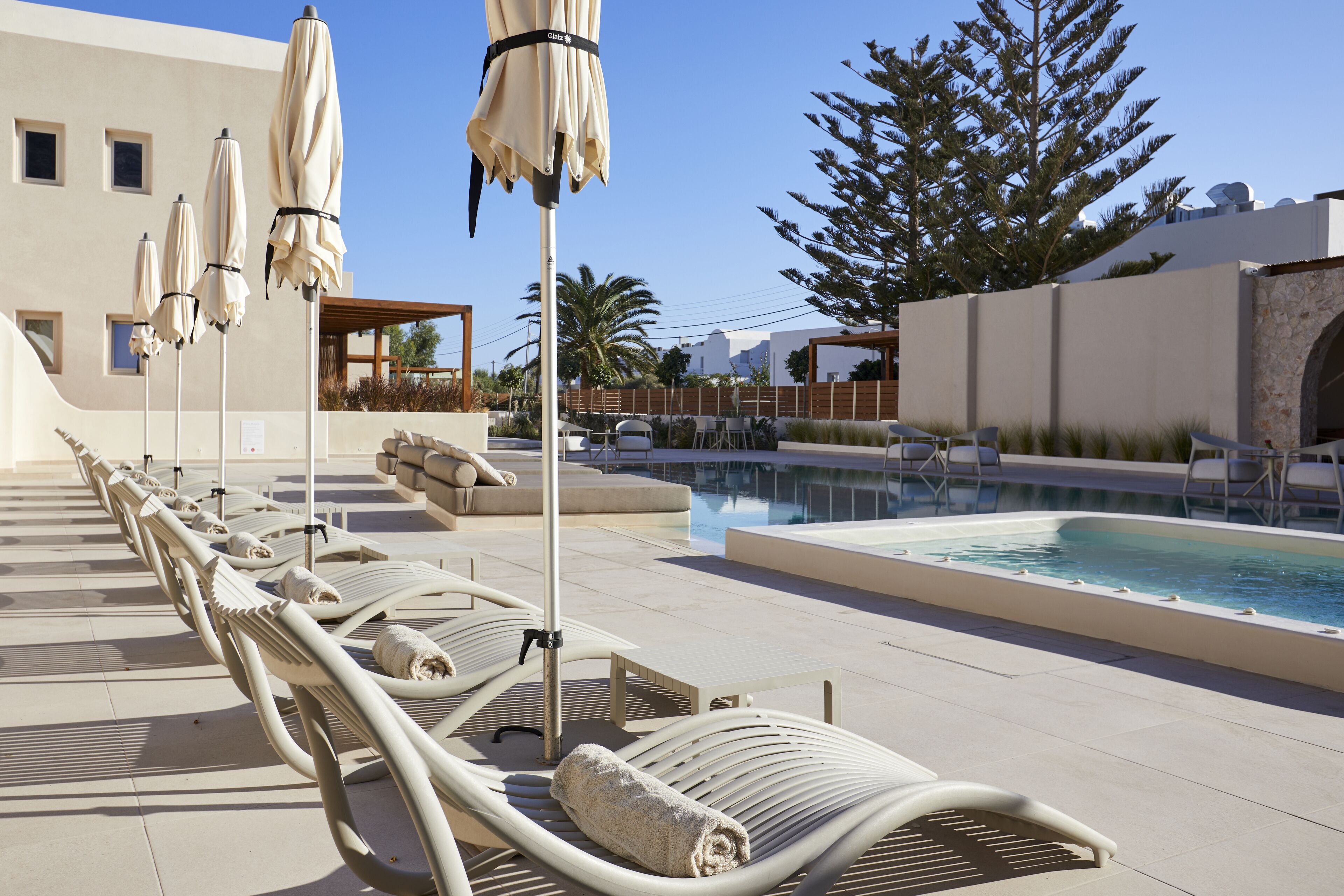 A poolside area with lounge chairs and umbrellas, a swimming pool, and a building with a modern design.
