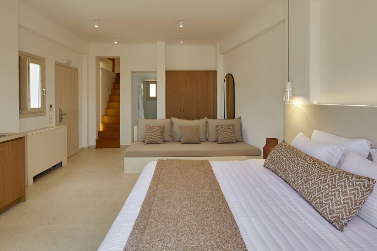A bedroom with a bed, a sofa, a staircase, and a desk.