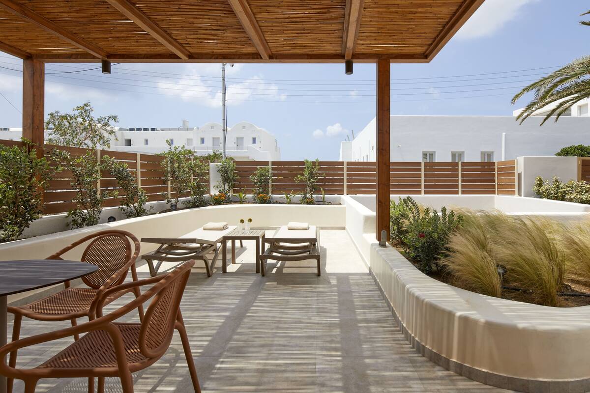 An outdoor patio with wooden furniture, a pool, and a view of white buildings in the background.