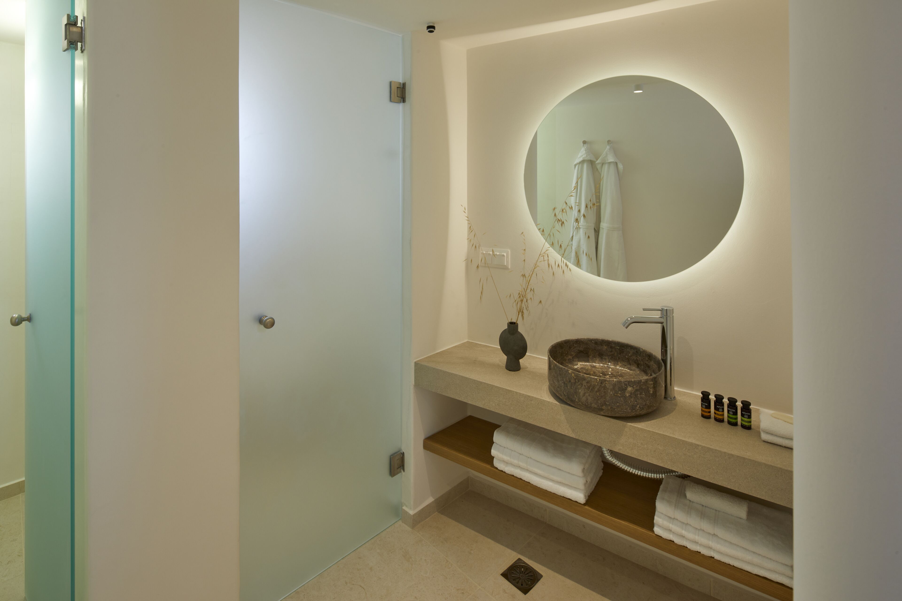 Een moderne badkamer met een ronde spiegel, een stenen wastafel en een handdoekhouder.
