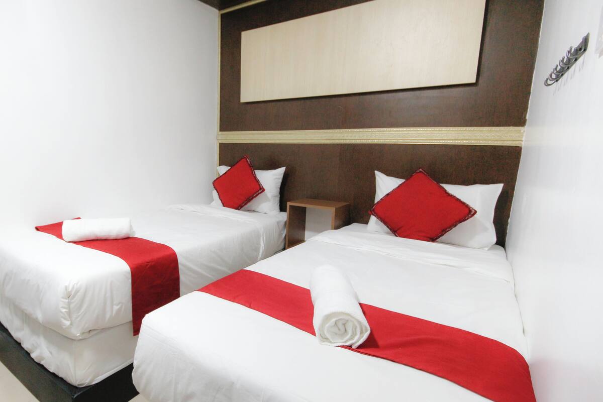 Two single beds with white and red bedding, a wooden nightstand, and a large mirror on the wall.