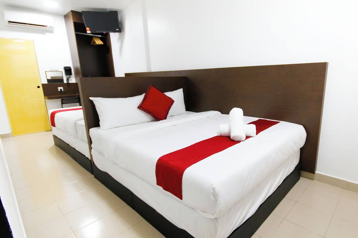 A hotel room with a large bed, a wooden headboard, and a red and white bedspread.