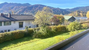 Zona residencial com uma casa de telhado cerâmico e um mural, cercada por vegetação exuberante e montanhas ao fundo.