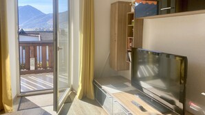 Quarto com porta de vidro deslizante para uma varanda, televisão de tela plana, armário de madeira e uma pequena estante com livros.