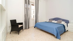 Un dormitorio con una cama, una silla, una mesita de noche y una puerta con cortinas.
