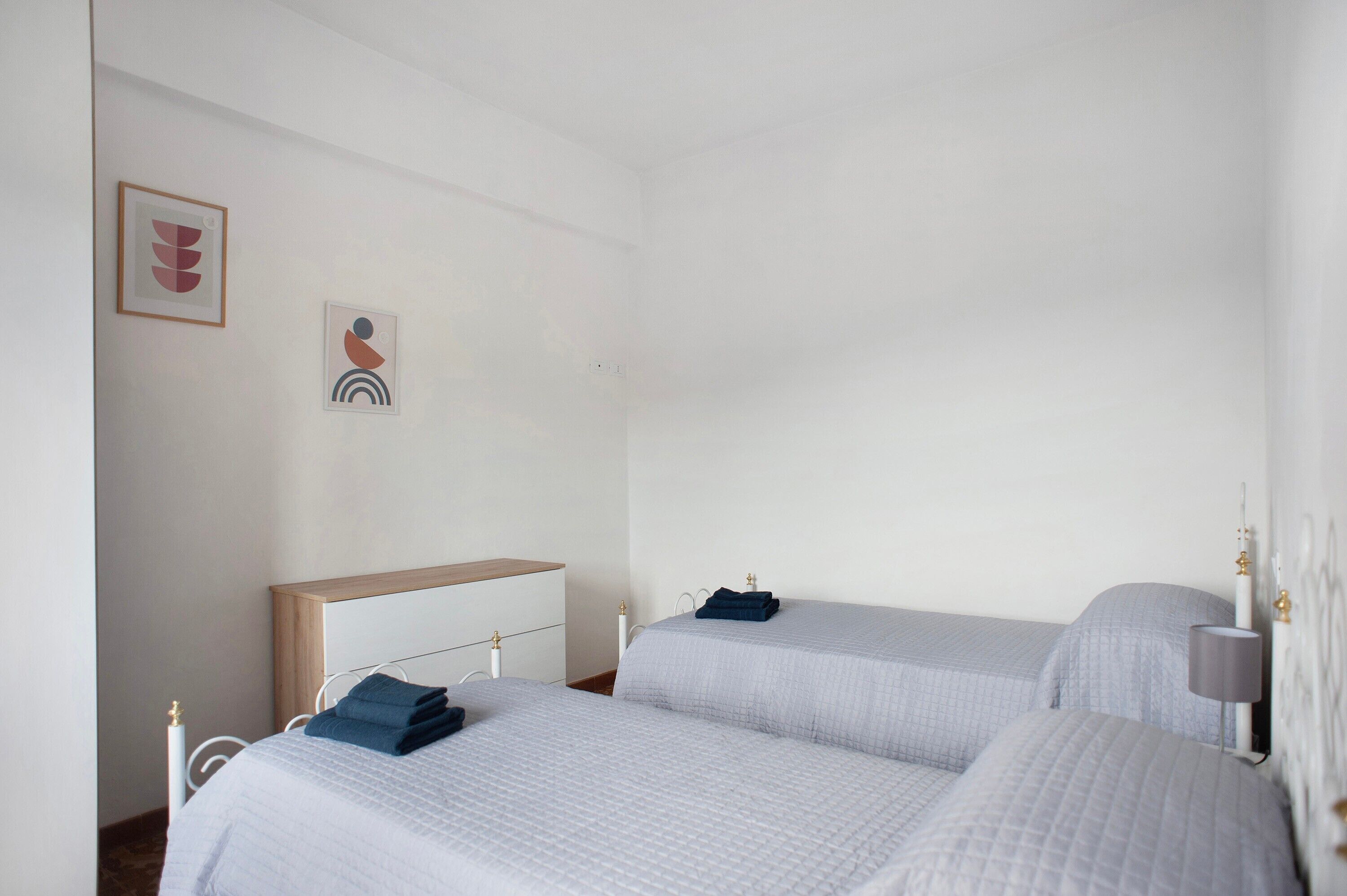 A hotel room with two beds, a bedside table, a lamp, and two wall-mounted artworks.