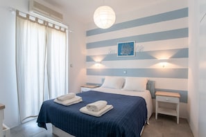 A bedroom with a bed, two bedside tables, a wall-mounted light, and a window with curtains.