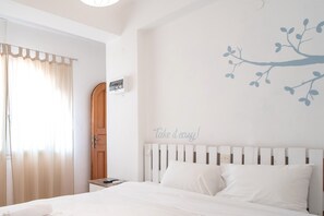 A bedroom with a bed, a nightstand, a wall-mounted air conditioning unit, a door, and a wall decal.