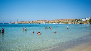 Une plage avec une eau claire, des gens qui se baignent et des bâtiments en arrière-plan.