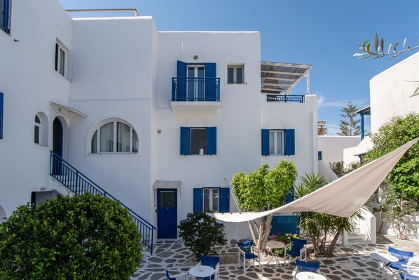 A courtyard with white buildings, blue shutters, and outdoor seating. - Studio Apartment 'Livadia Seaside Studios 11' with Shared Terrace, Wi-Fi and Air Conditioning (Paros)
