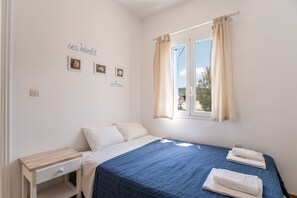 A bedroom with a bed, a bedside table, a window with curtains, and wall decorations. - Studio Apartment 'Livadia Seaside Studios 11' with Shared Terrace, Wi-Fi and Air Conditioning (Paros)