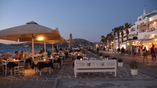 A seaside restaurant with outdoor seating, a white bench, and a view of the sea and hills. - Studio Apartment 'Livadia Seaside Studios 12' with Shared Terrace, Wi-Fi and Air Conditioning (Paros)