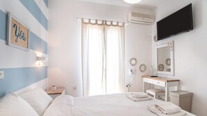 A hotel room with a bed, a vanity with a mirror, a flat-screen TV, and a window with curtains.