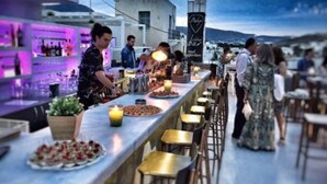 A rooftop bar with a long counter, bar stools, and a view of the cityscape.