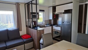 A compact kitchenette with a microwave, stove, and refrigerator, a sofa with a red pillow, and a small dining table.
