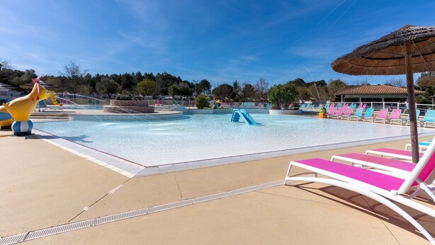 A swimming pool area with lounge chairs, a water slide, and a thatched umbrella.