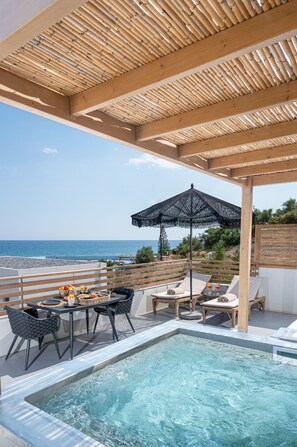 Zona de piscina en la azotea con vista al mar, pérgola de madera y mobiliario exterior.