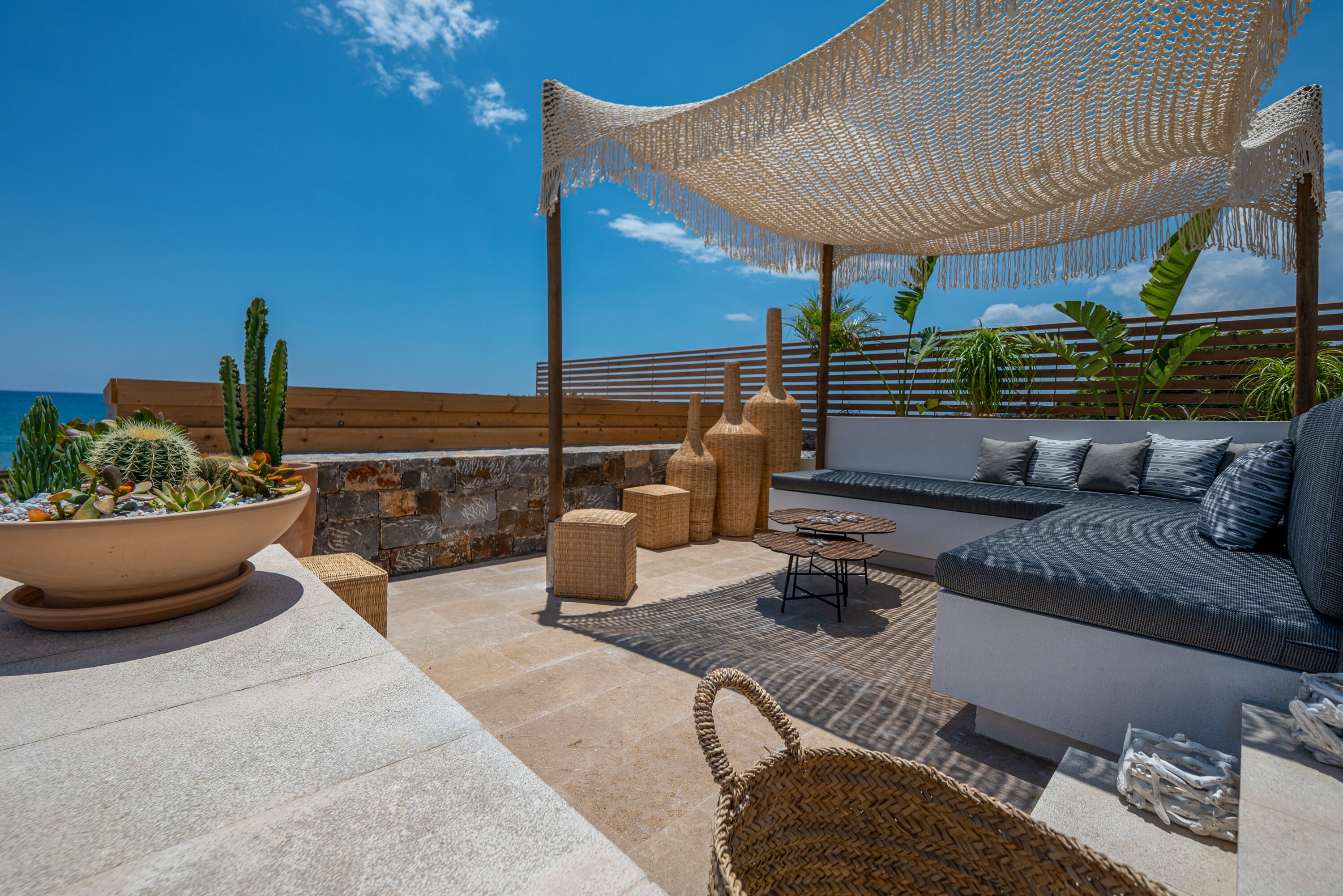 A rooftop terrace with a seating area, a large woven umbrella, and potted plants.