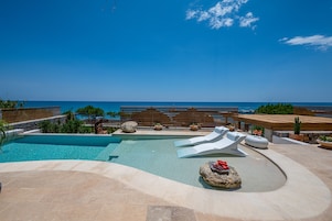 Zona de piscina con vista despejada al océano, sillas de descanso y una terraza de madera.