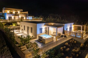 Una casa moderna de varios pisos con piscina, mobiliario exterior y un patio bien iluminado.