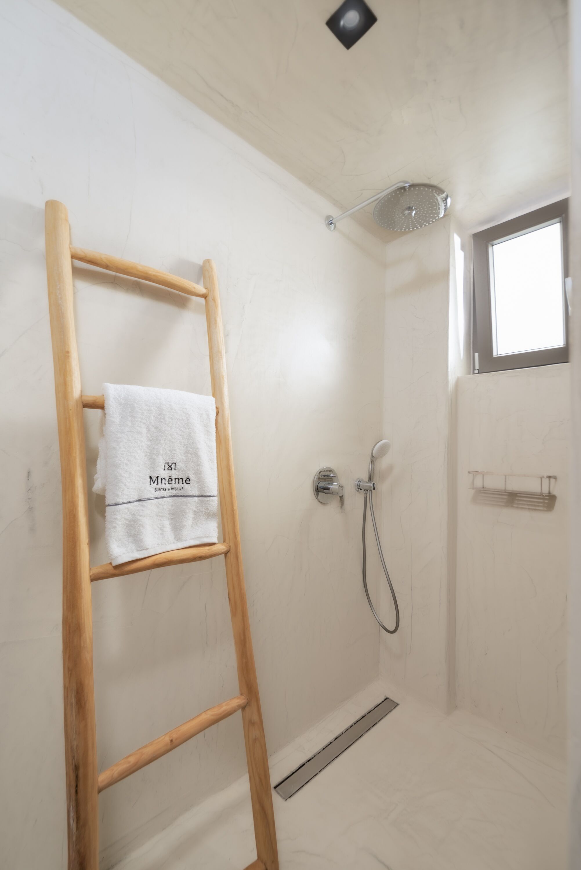 A shower area with a wooden ladder, a towel hanging on it, and a window above the shower.
