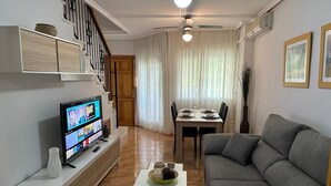 A living room with a TV, sofa, dining table, and staircase. - Bungalow 'Villa Matías' with Sea View, Wi-Fi and Air Conditioning (Gran Alacant)