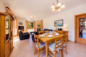 A dining area with a wooden table set for four, a sofa, a television, and a fireplace.