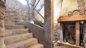 Eine Steintreppe führt zu einem Kamin, über dem sich ein Regal mit verschiedenen Gegenständen befindet.