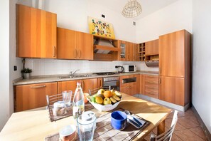 A kitchen with wooden cabinets, a dining table with a bowl of fruit, and a microwave.
