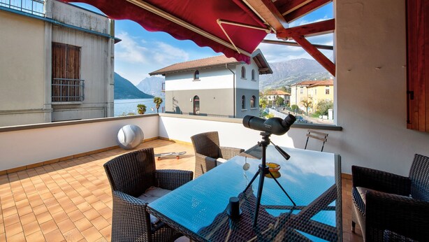 A terrace with wicker furniture, a telescope, and a view of mountains. - Holiday Home 'Wakesurfhouse 2' with Lake View, Private Terrace and Wi-Fi (Sulzano)