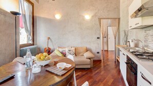 A kitchen with a stove, a dining table with a bowl of fruit, a sofa, and a guitar. - Holiday Home 'Wakesurfhouse 2' with Lake View, Private Terrace and Wi-Fi (Sulzano)