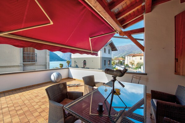 Un balcon agrémenté de meubles en osier, d’un télescope et d’un parasol rouge.