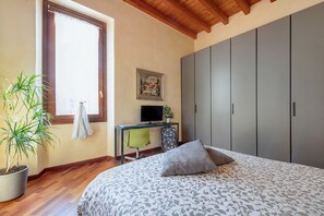 A bedroom with a bed, a desk with a chair, a television, a wardrobe, and a potted plant.